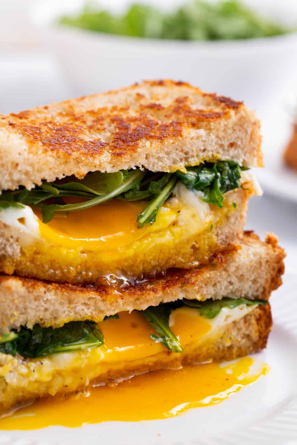 close up image of the cross section of a fried egg and cheese sandwich served on a white round plate