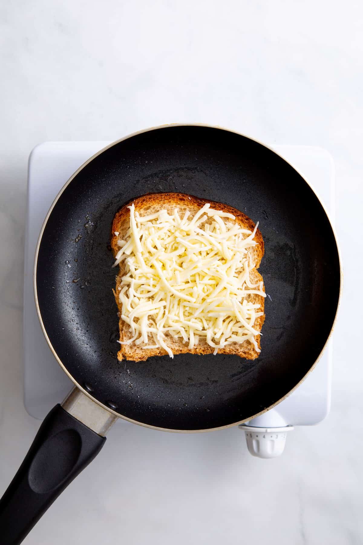 butter slice of white bread on a skillet topped with shredded cheese