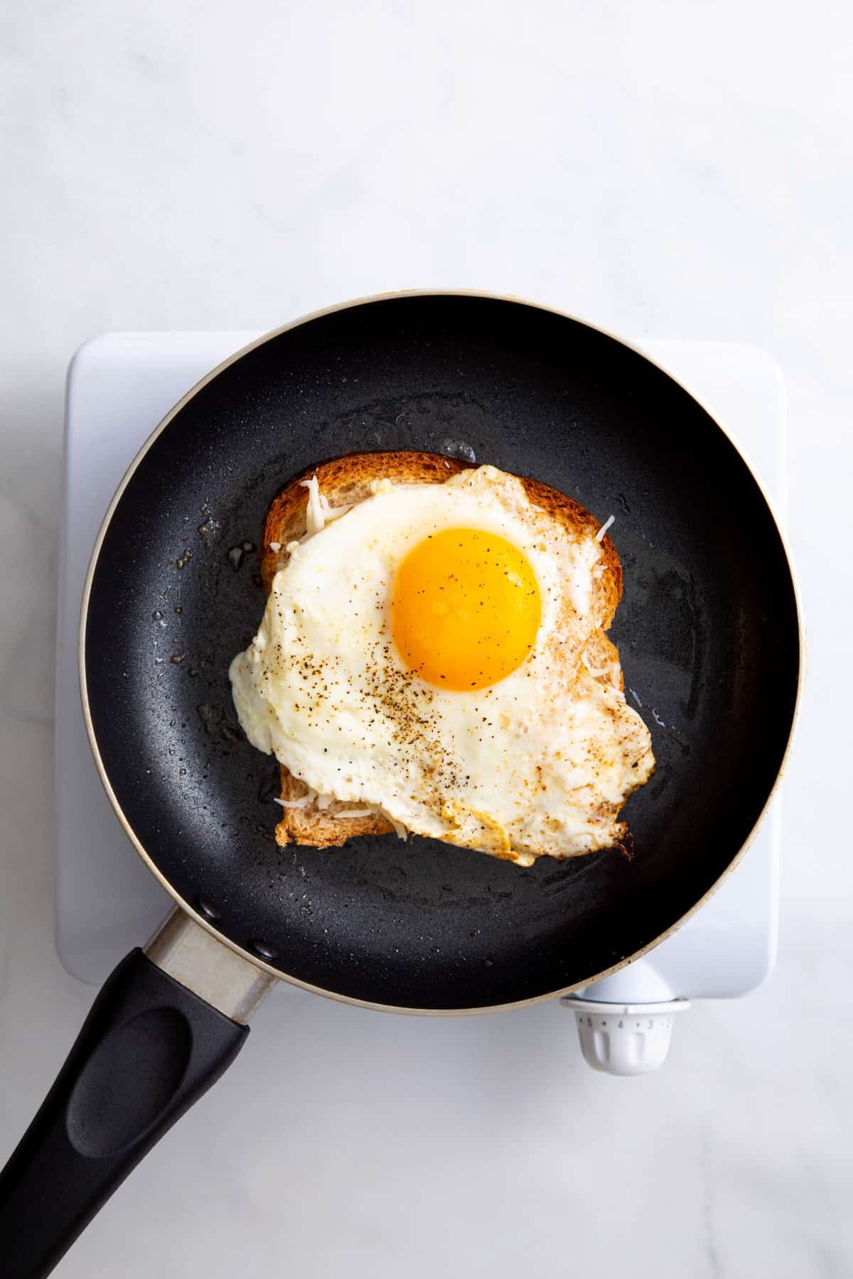 butter slice of white bread on a skillet topped with shredded cheese and a fried egg