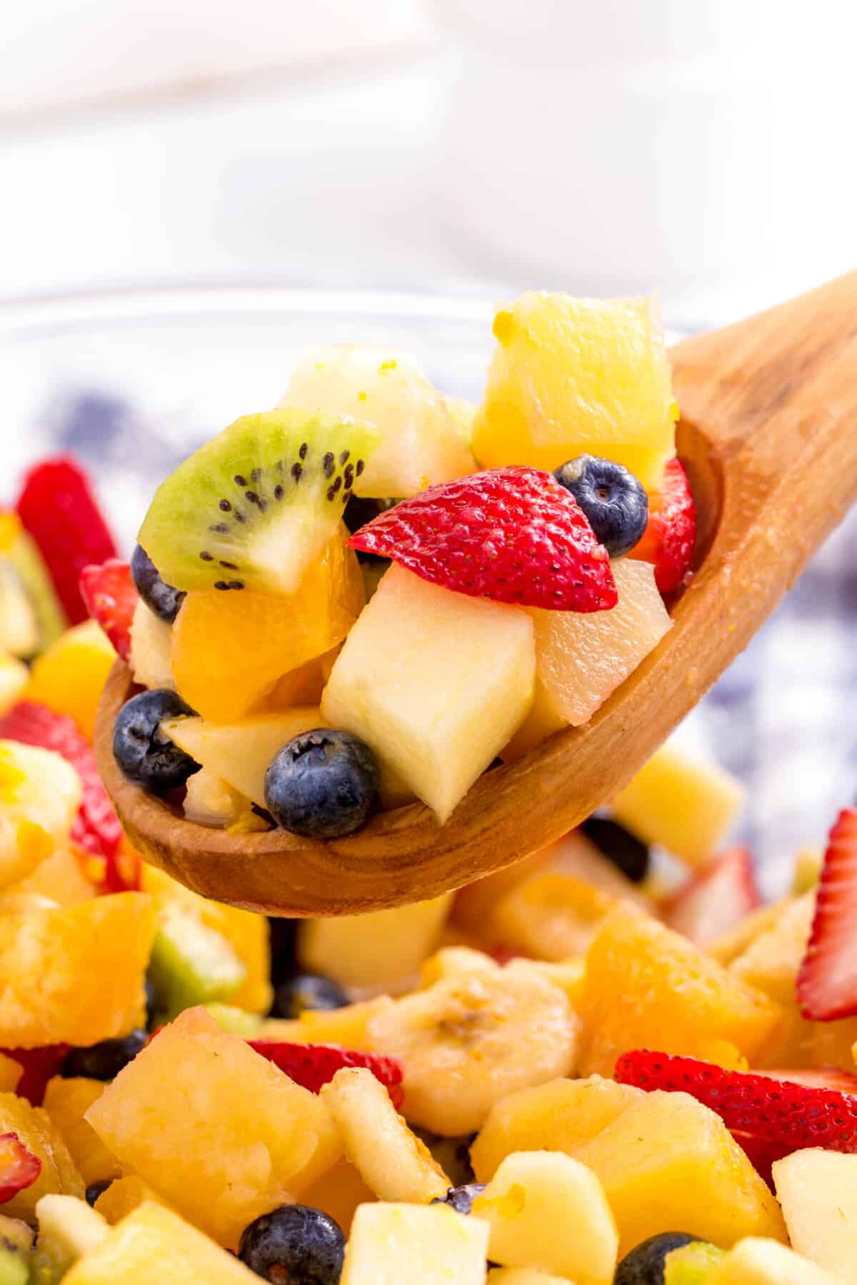 A wooden spoon lifting a scoop of fruit salad from a bowl.