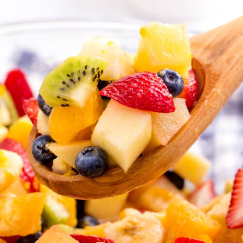A wooden spoon lifting a scoop of fruit salad from a bowl.