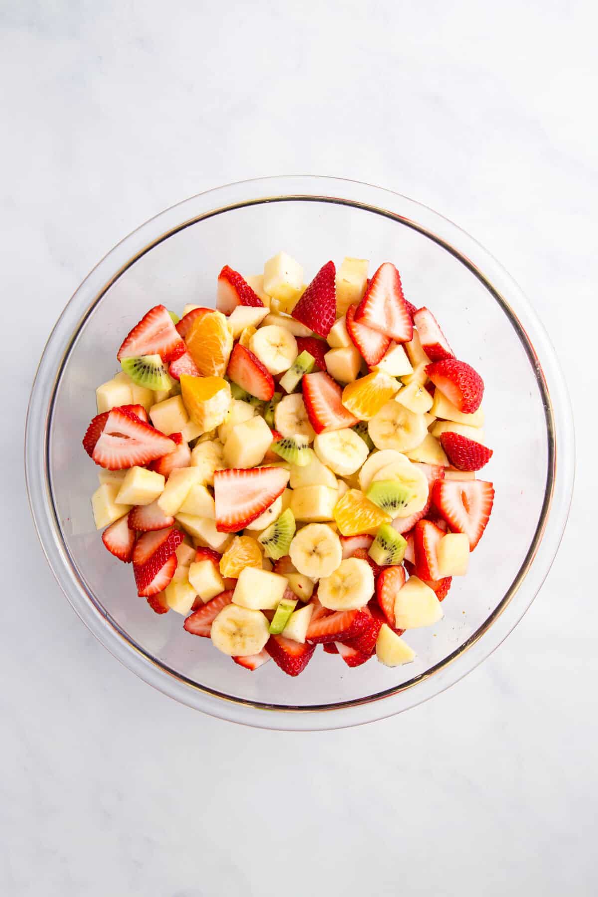 cut up strawberries, bananas, kiwi, oranges in a large glass bowl.