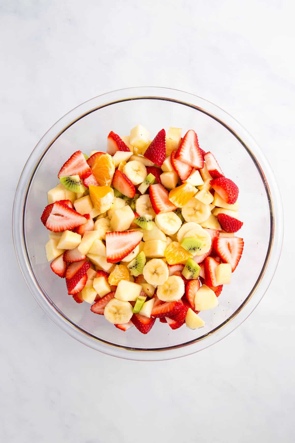 cut up strawberries, bananas, kiwi, oranges in a large glass bowl