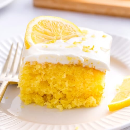 A slice of lemonade cake with lemon frosting and a lemon slice on top.
