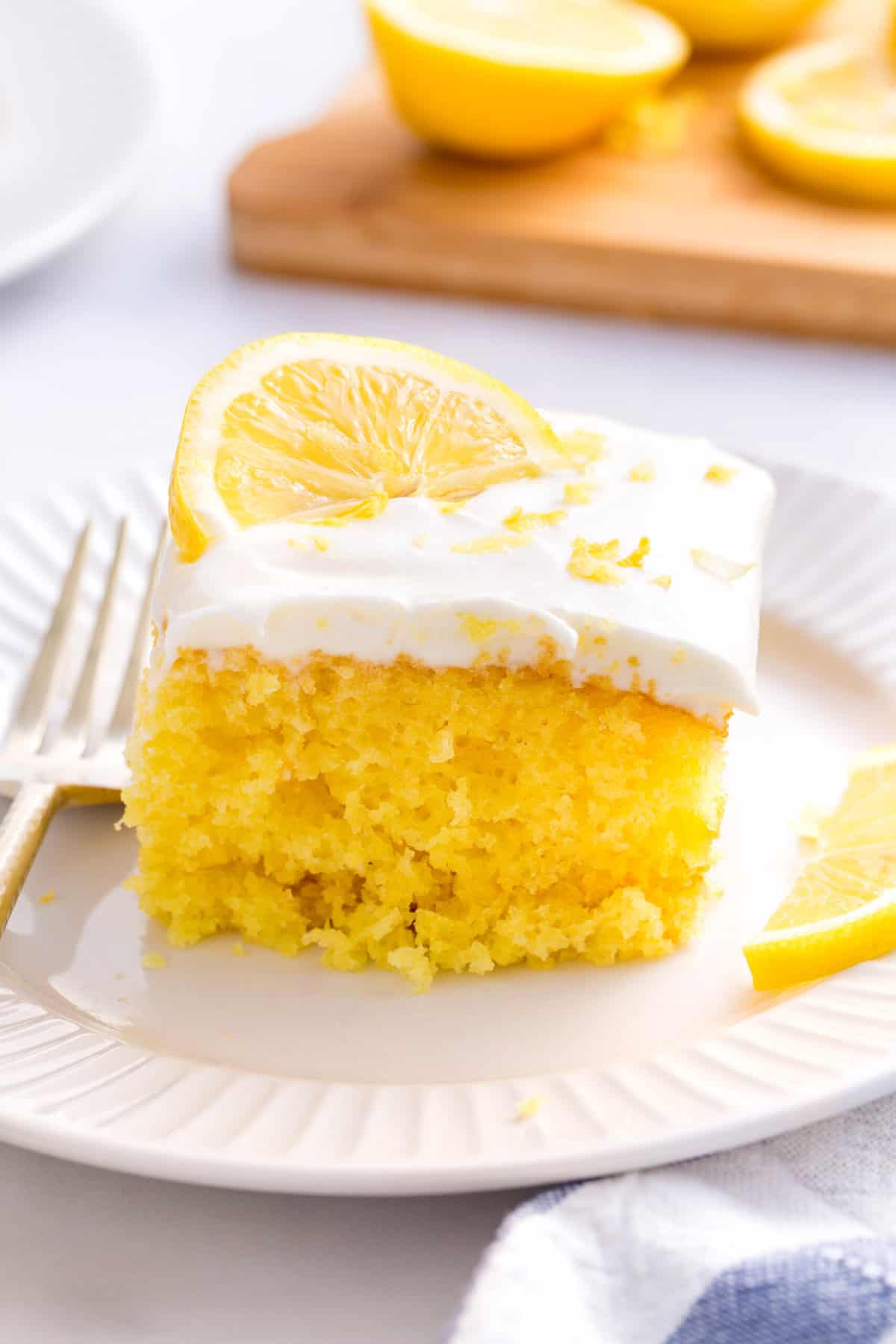 lemonade cake topped with frosting and a fresh lemon slide sitting on a white round plate