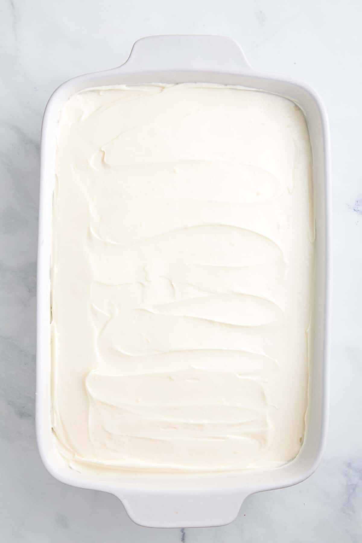 baked lemonade cake topped with frosting sitting in a 9x13 casserole baking dish.