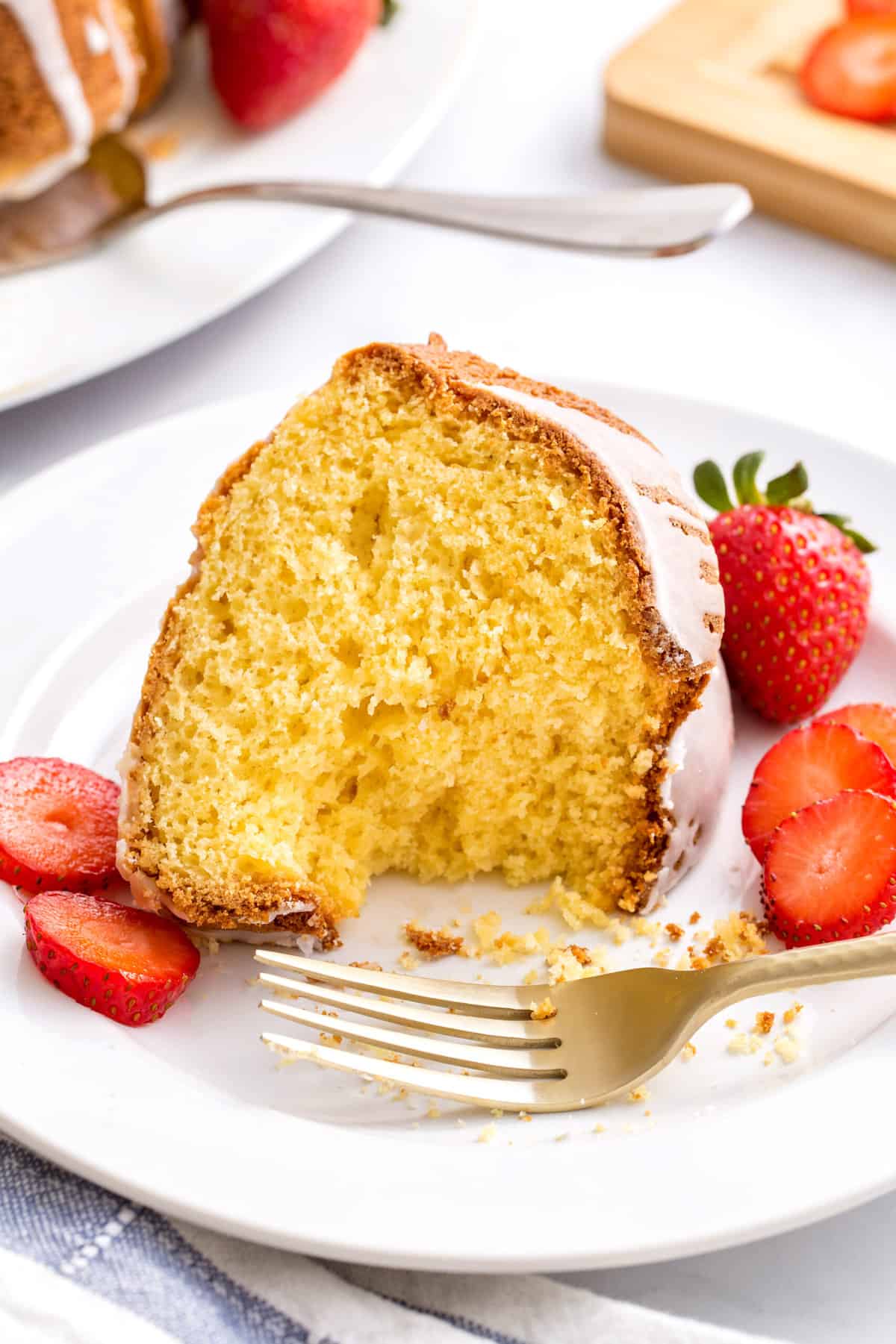 slice of cake mix pound cake served on a white round plate with cut fresh strawberries on the side