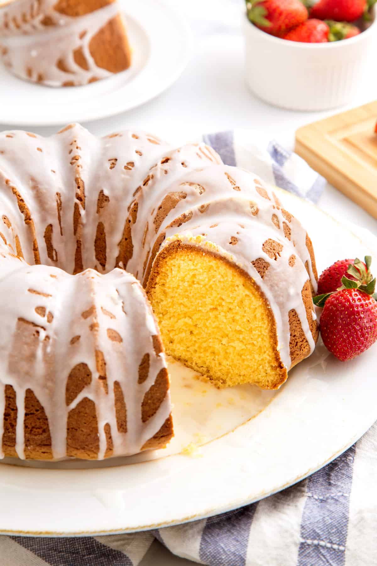 cake mix pound cake in the shape of a bundt, topped with a lemon glaze with two fresh strawberries on the side all served on a white round plate