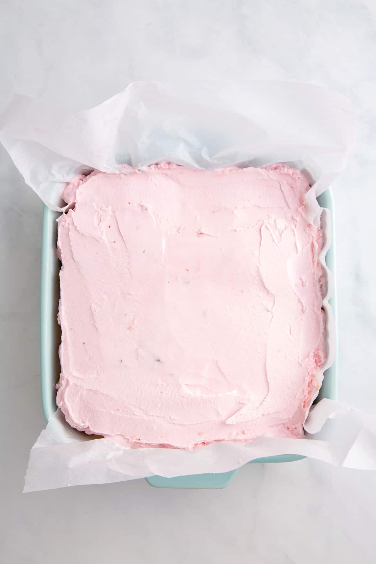 strawberry ice cream layered on top of an 8x8 dish to make strawberry crunch ice cream cake