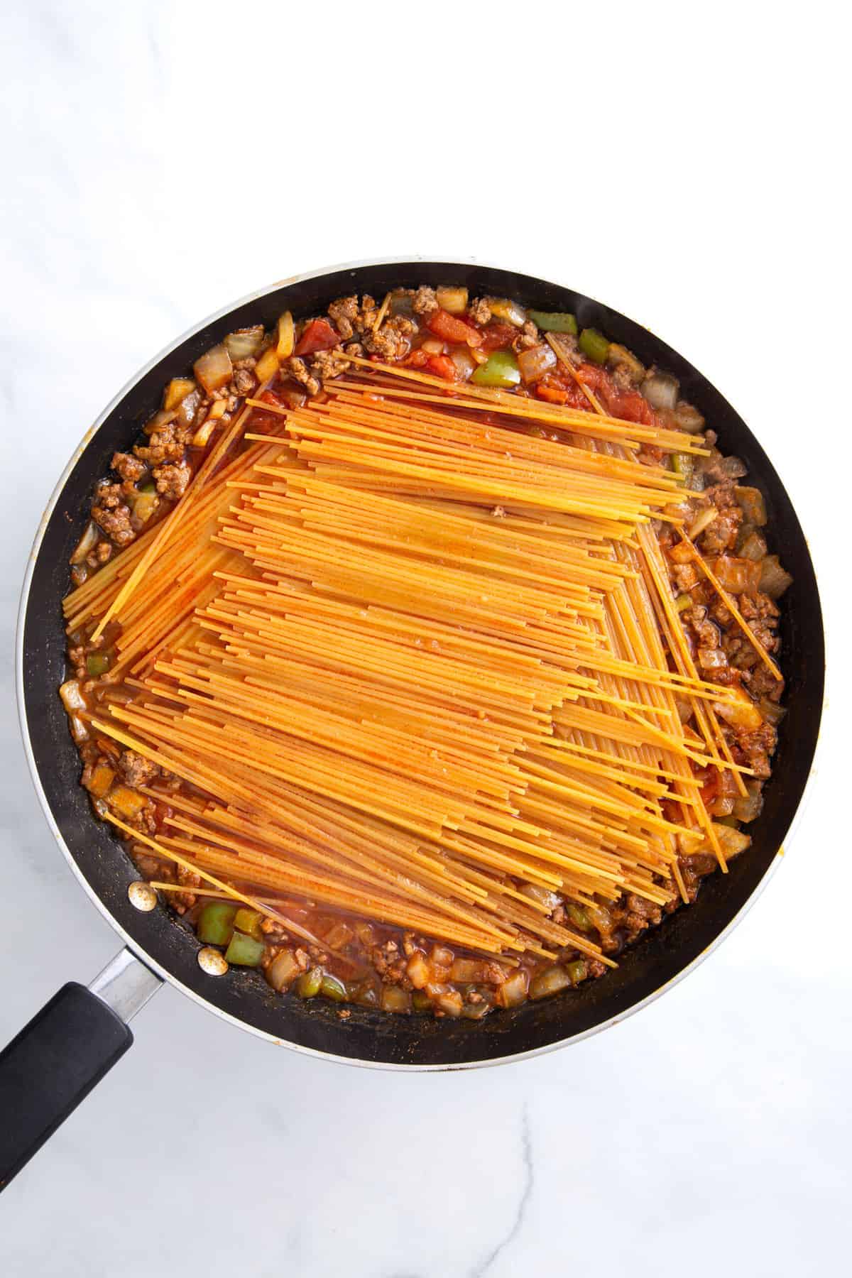 large pane of uncooked spaghetti noodles layered on top of taco meat