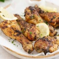 close up image of air fryer chicken drumsticks served on a plate topped with lemon slices and parsley