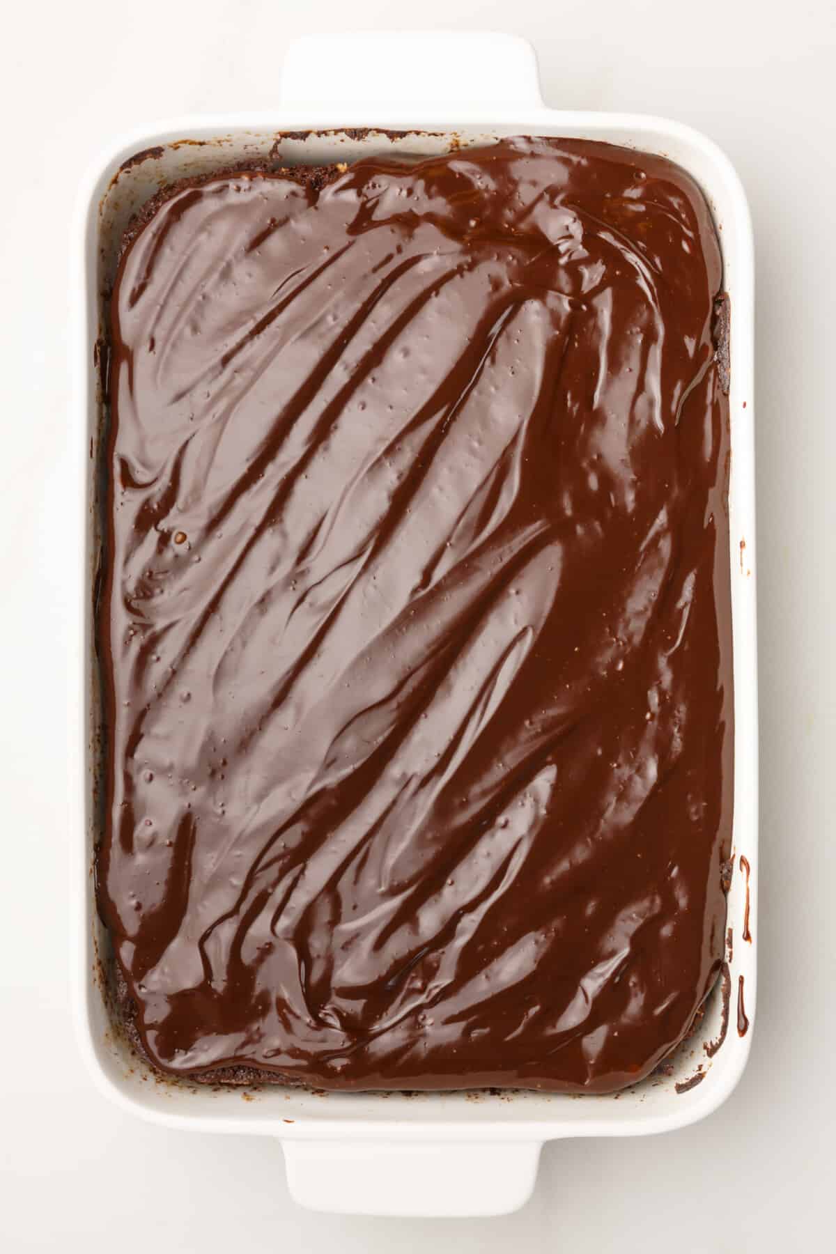 chocolate ganache spread on top of chocolate zucchini cake sitting in a 9x13 baking dish