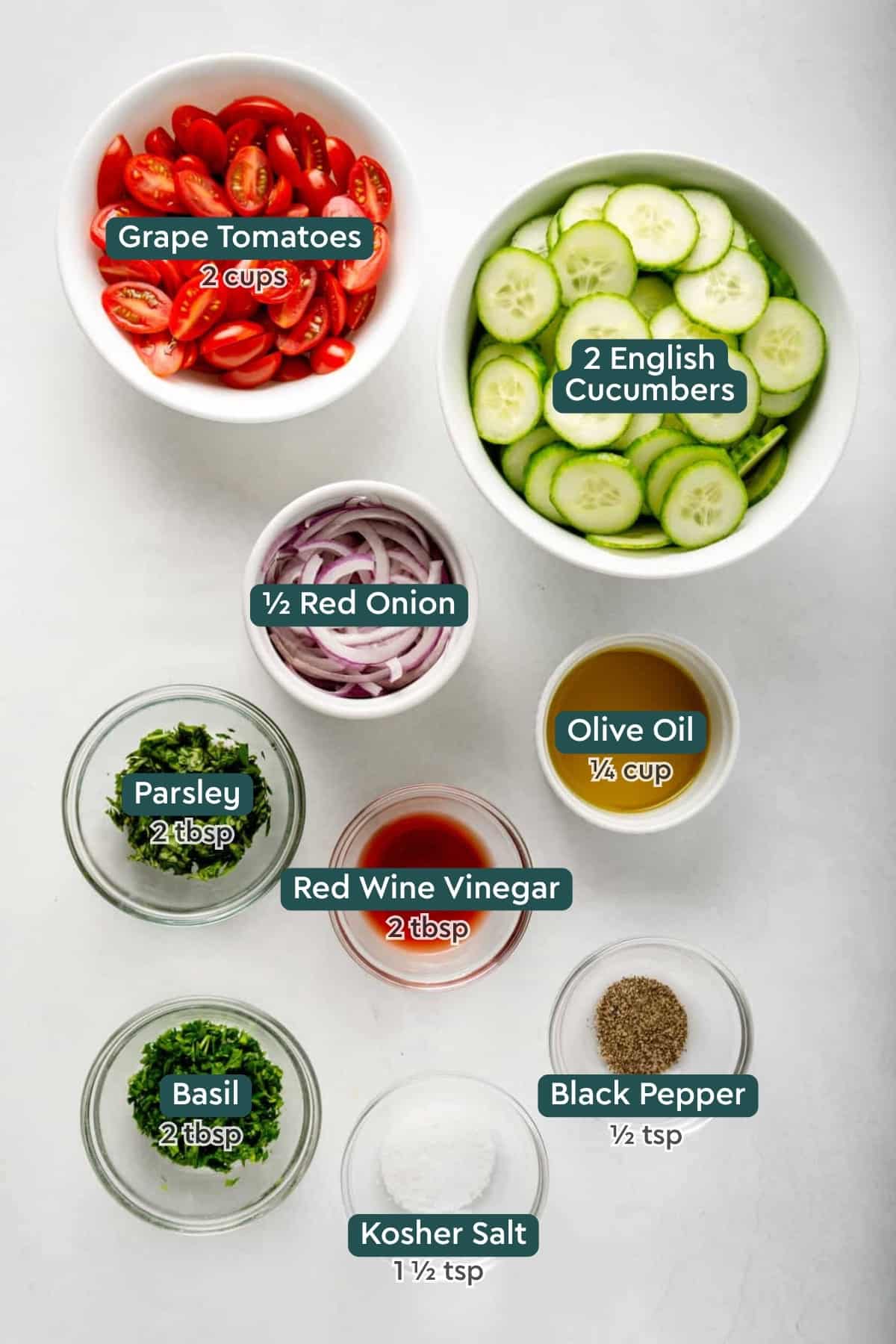 Ingredients for cucumber tomato salad, including tomatoes, cucumbers, red onion, olive oil, parsley, red wine vinegar, basil, salt, pepper.