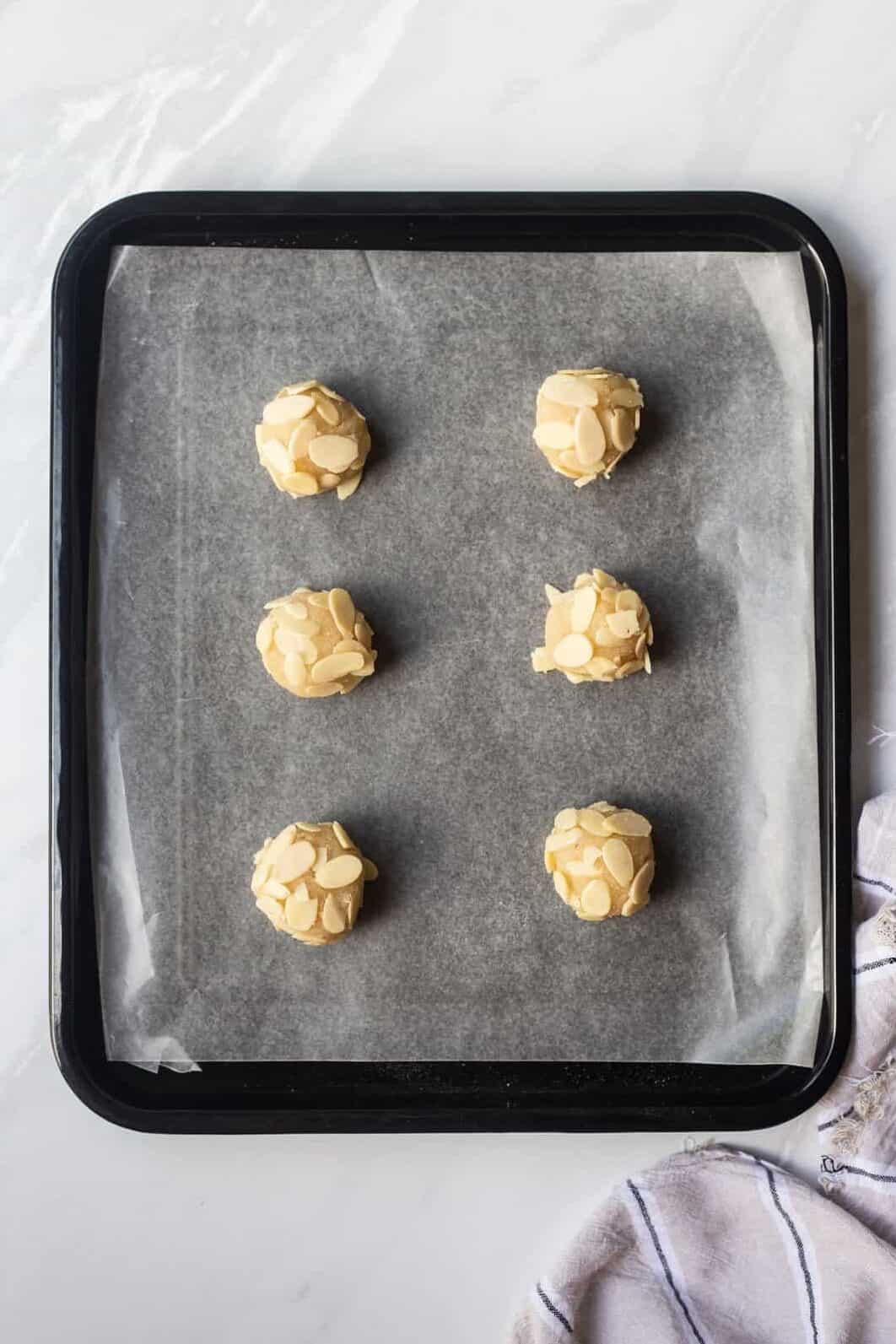 parchment lined baking sheet with six almond cookie dough balls.
