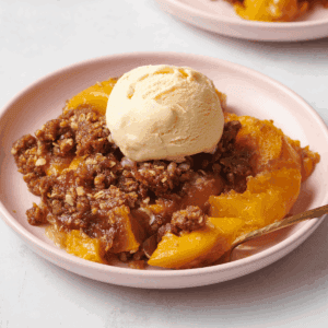 A plate of peach crisp topped with vanilla ice cream.