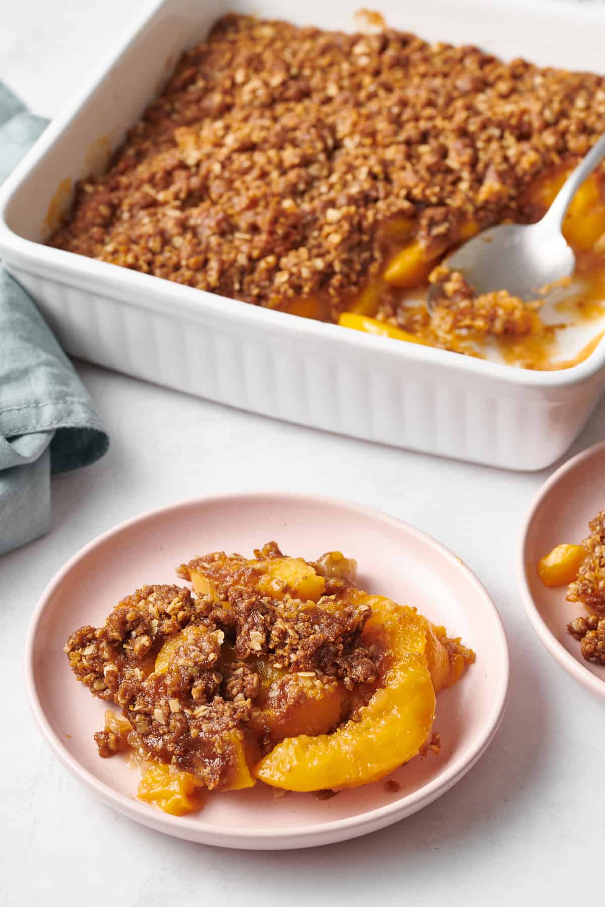 light pink plate of peach crisp and the casserole dish in the background