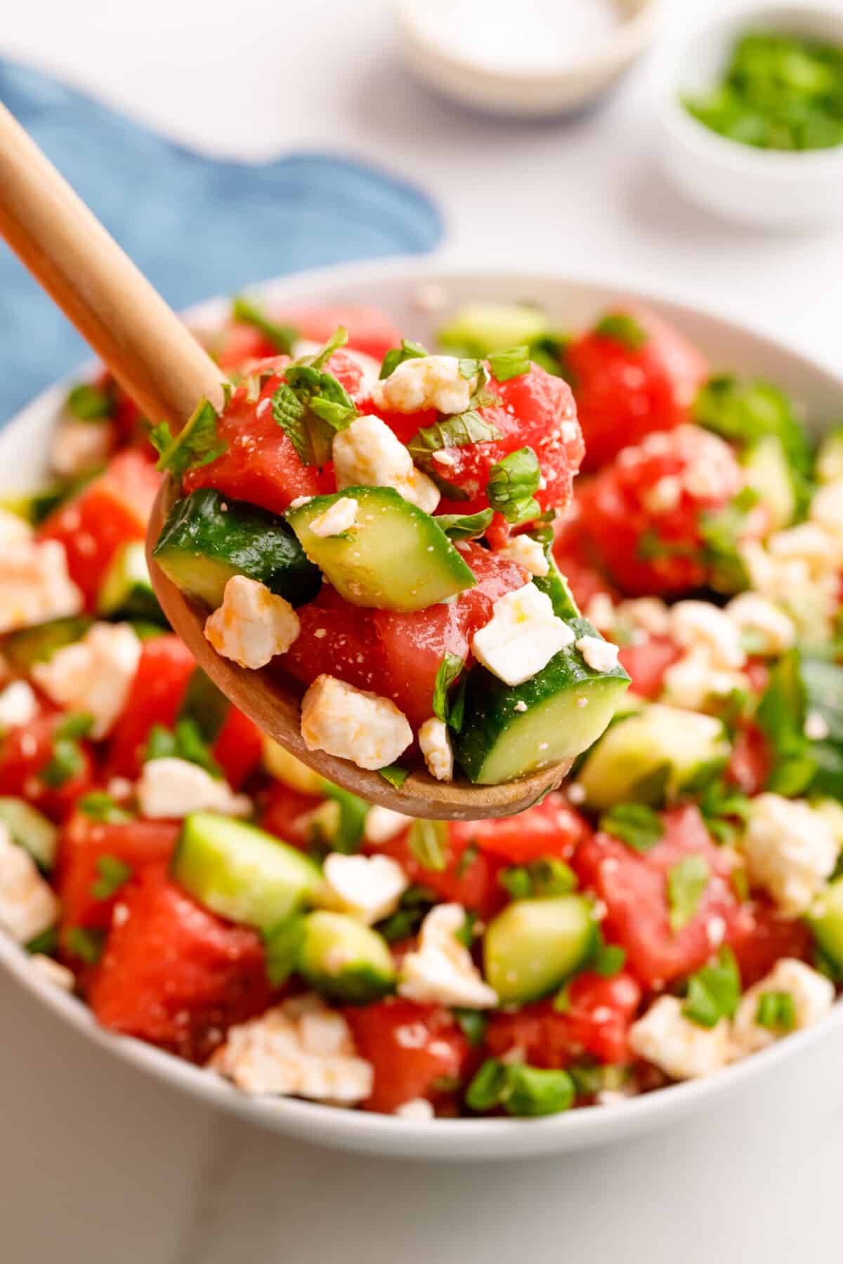 A spoon lifting a scoop of watermelon and feta salad from a bowl.