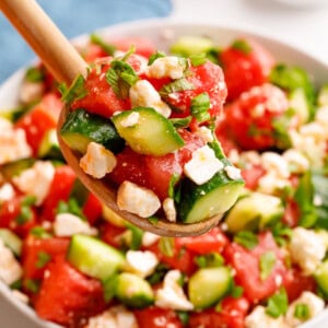A spoon lifting a scoop of watermelon and feta salad from a bowl.