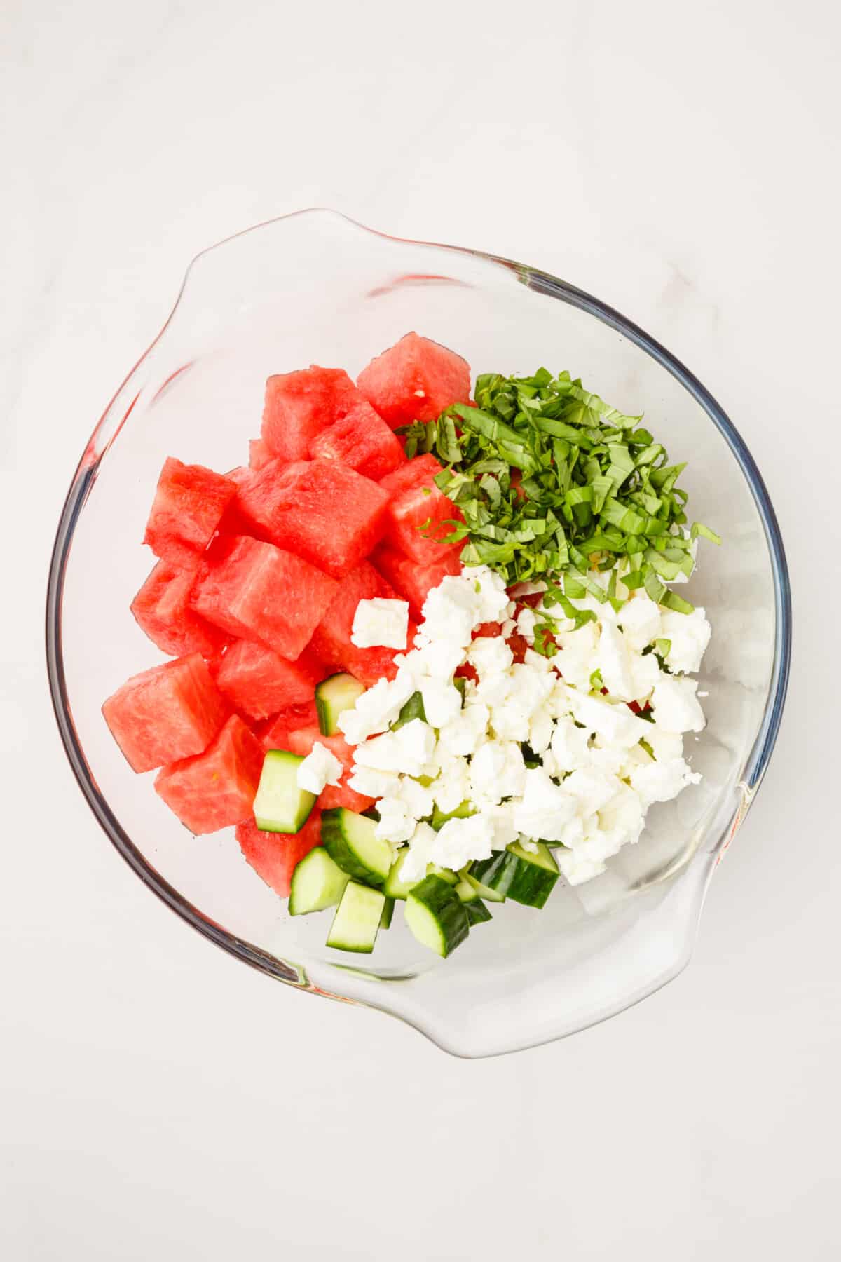 cubed watermelon, cut mint, cucumbers and feta cheese unmixed in a large glass bowl.