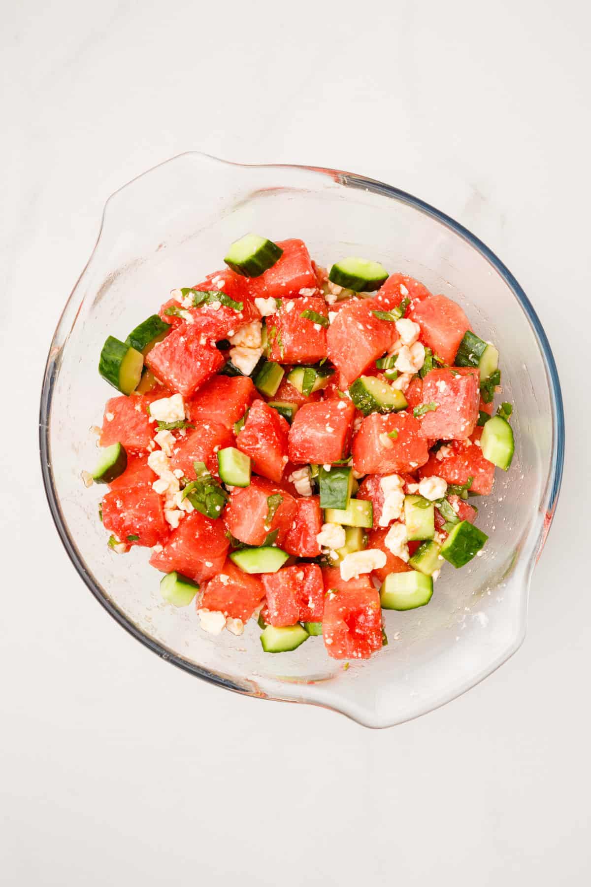 cubed watermelon, cut mint, cucumbers and feta cheese mixed in a large glass bowl