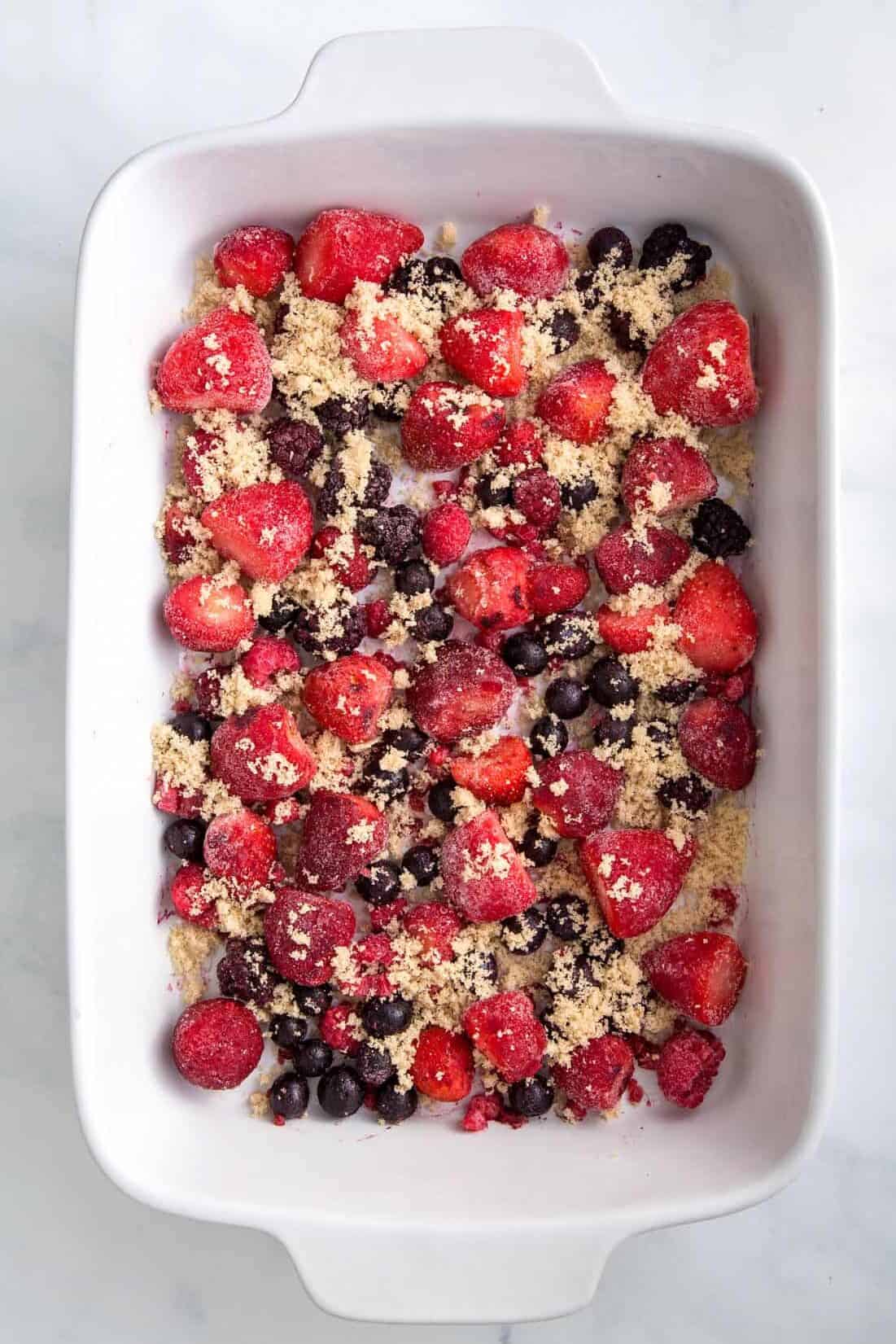 9x13 casserole dish with frozen berries spread evenly at the bottom and brown sugar sprinkled on top