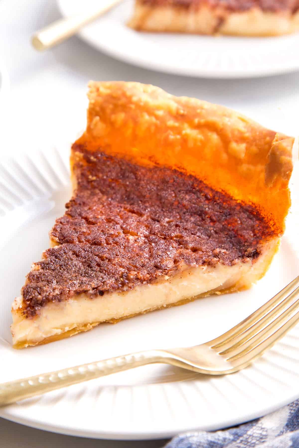 slice of custard pie sitting on a white round plate with a gold fork