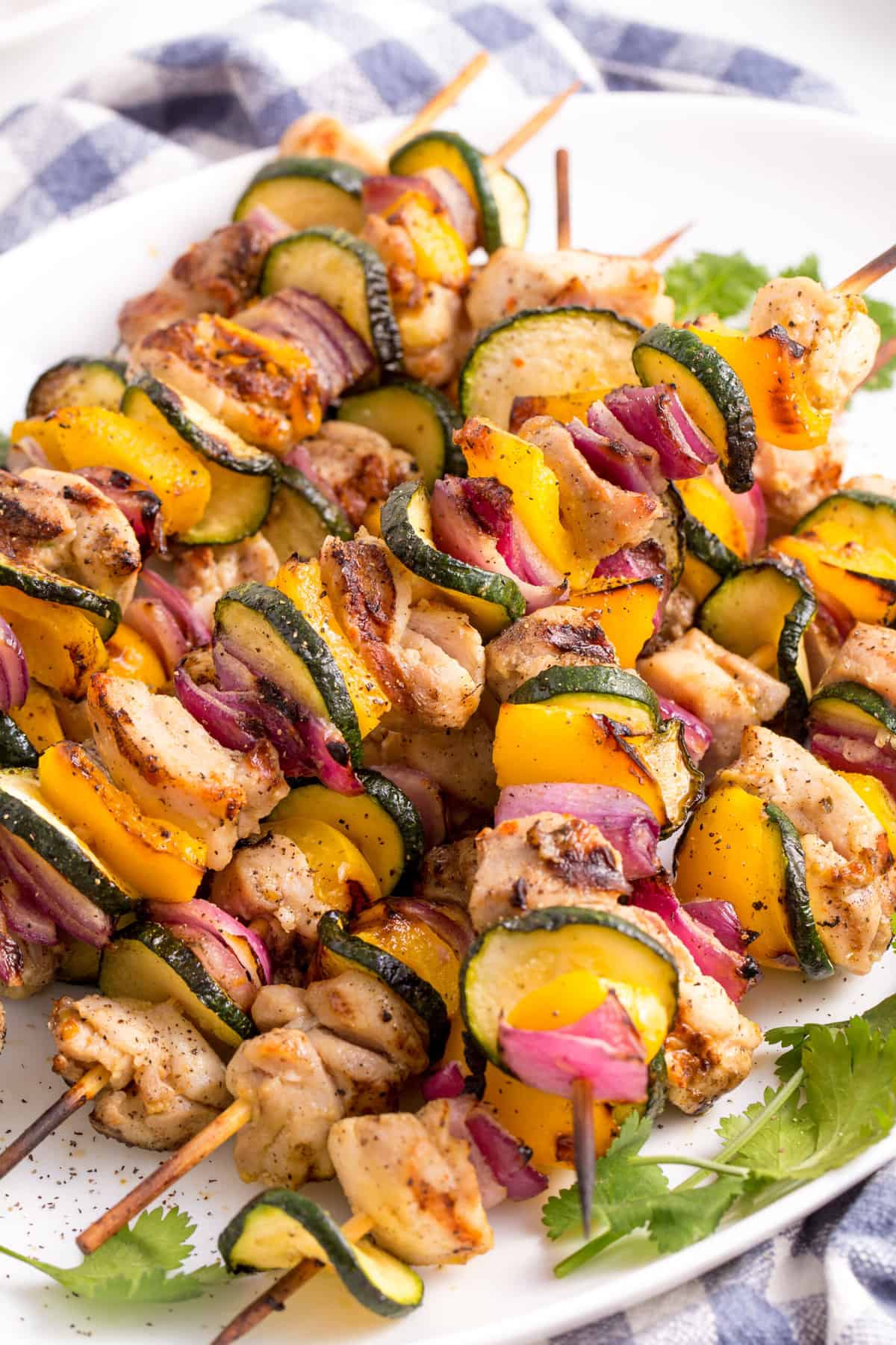 close up image of a pile of grilled chicken and vegetable kabobs served on a white oval plate