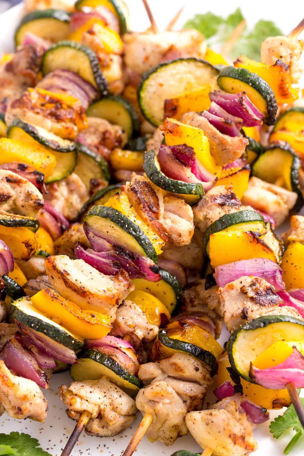 close up image of a pile of grilled chicken and vegetable kabobs served on a white oval plate