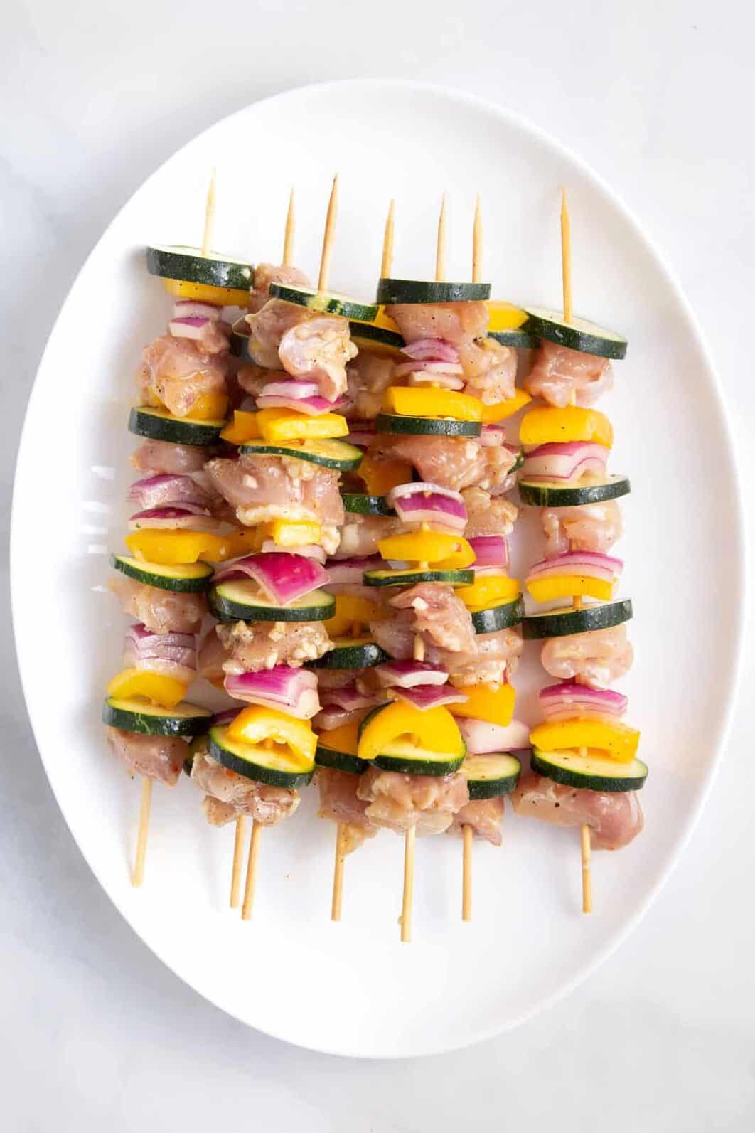 prepped and uncooked chicken and vegetable kabobs sitting on a white oval plate