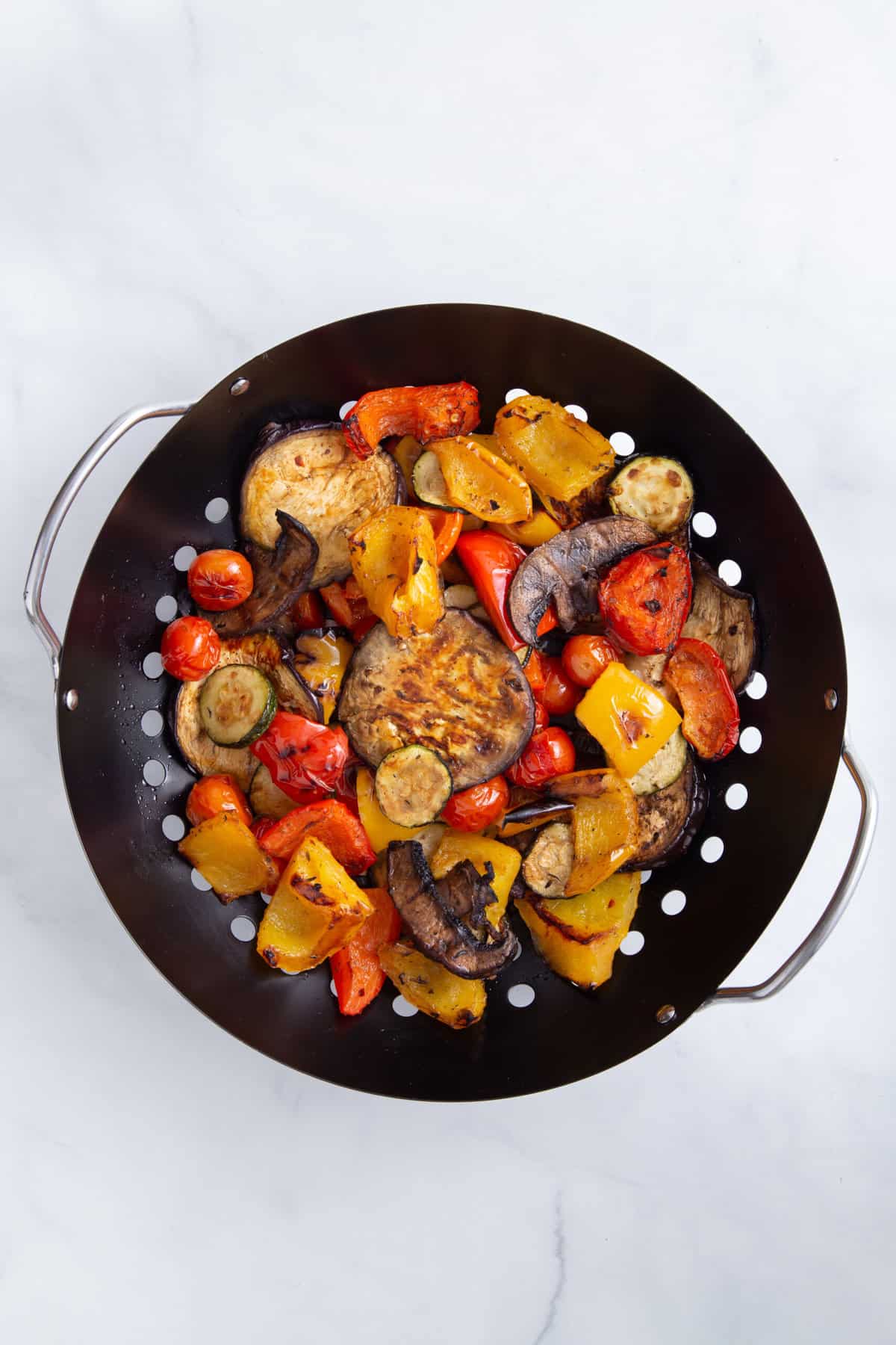 grilled vegetables tossed in marinade sitting in a large greased grill basket