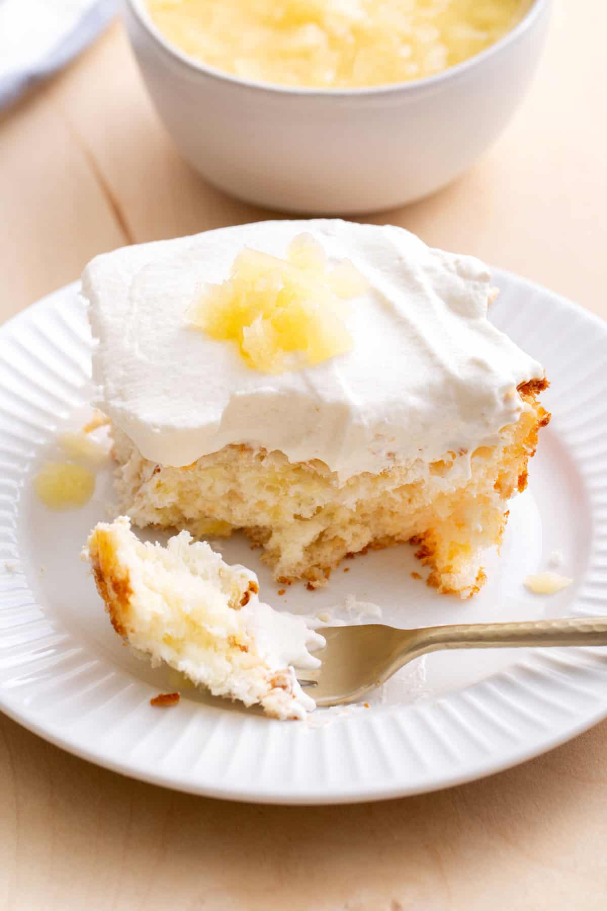 fork digging into a square serving of pineapple angel food cake served on a white round plate