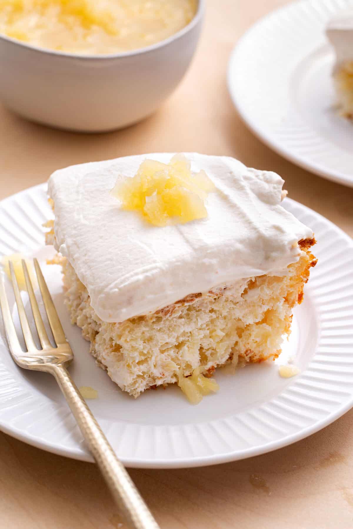 square slice of pineapple angel food cake sitting on a white round plate with a gold fork