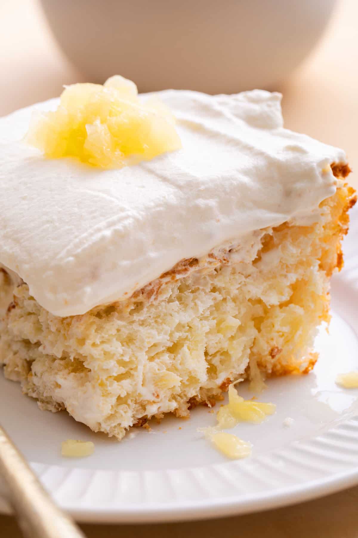 close up image of a square slice of pineapple angel food cake served on a white round plate