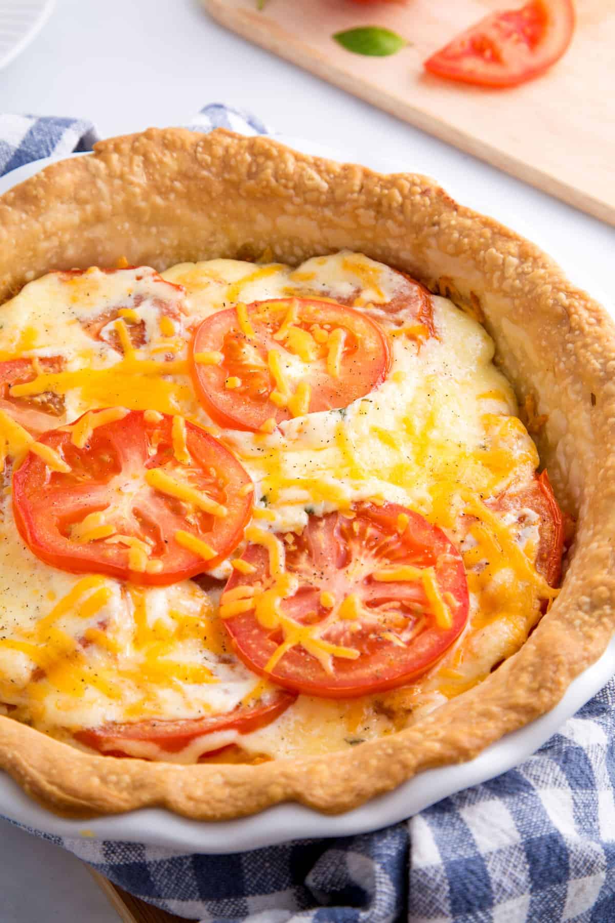 baked southern tomato pie sitting on a blue checkered kitchen towel