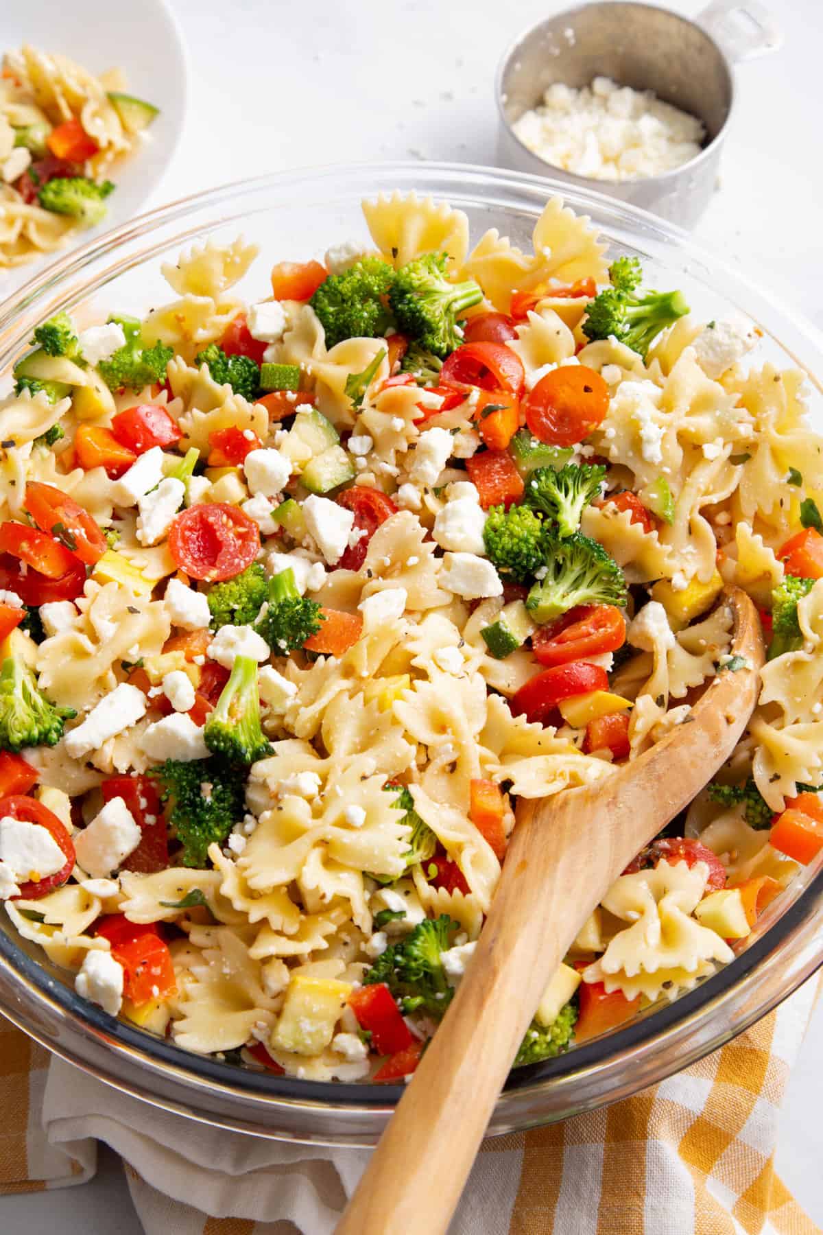 summer vegetable pasta salad in a large glass bowl with a wooden spoon