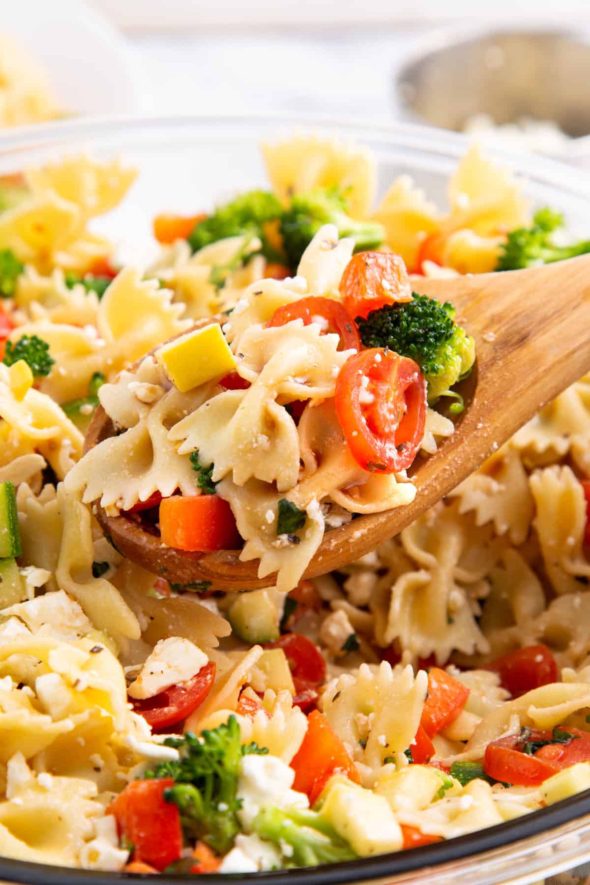 close up image of summer vegetable pasta salad on a wooden spoon