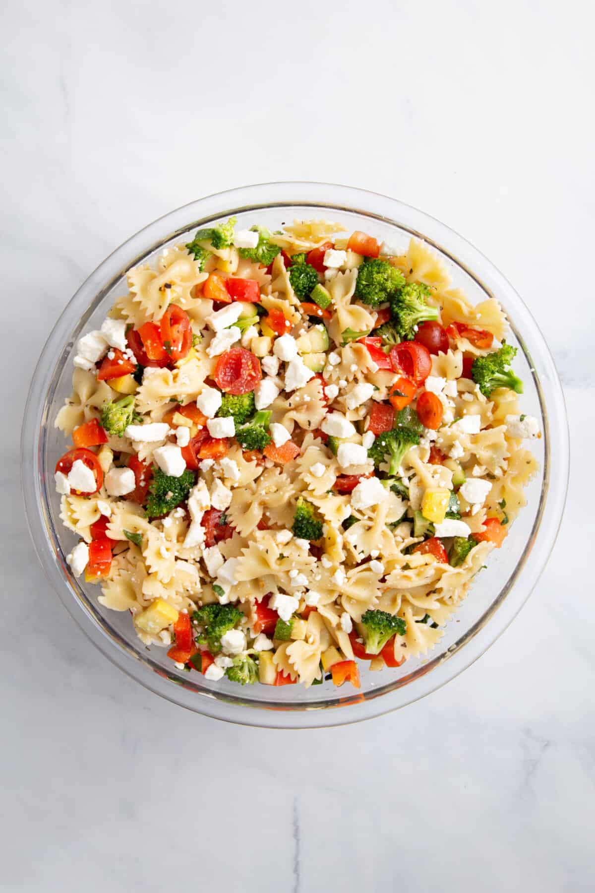summer vegetable pasta salad with feta cheese in a large glass bowl.