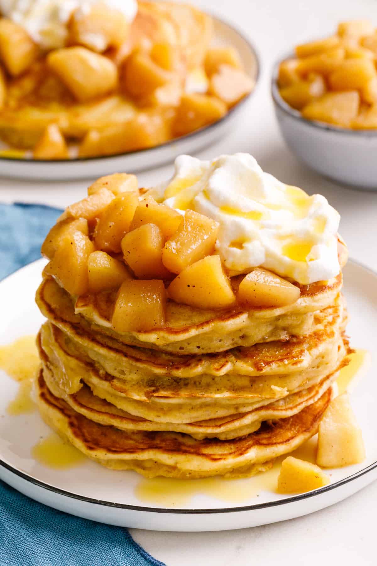 stack of five apple pancakes topped with chopped cooked granny smith apples, whipped cream and syrup