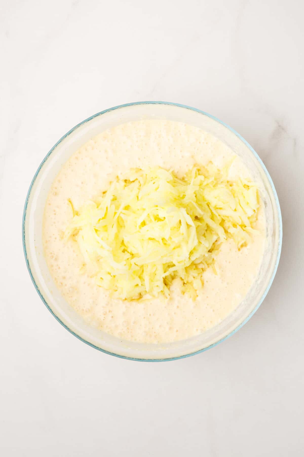 pancake batter and shredded granny smith apples not mixed in sitting in a large glass bowl.