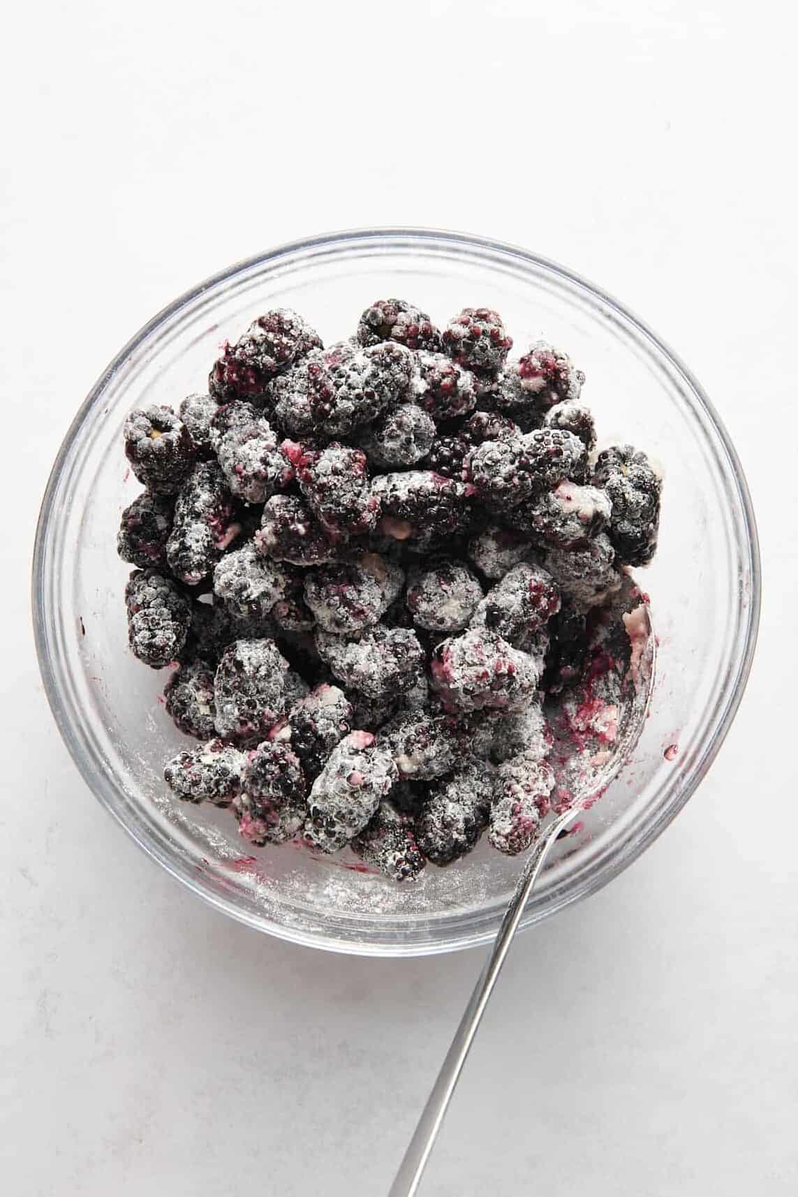 blackberries tossed and coated in a sugar, lemon, flour mixture sitting in a large glass bowl