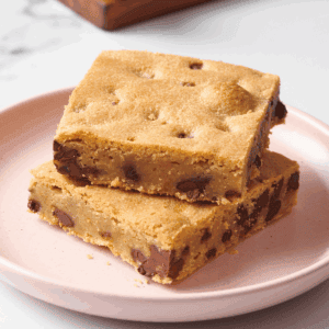 Two chocolate chip cookie bars stacked on a pink plate.
