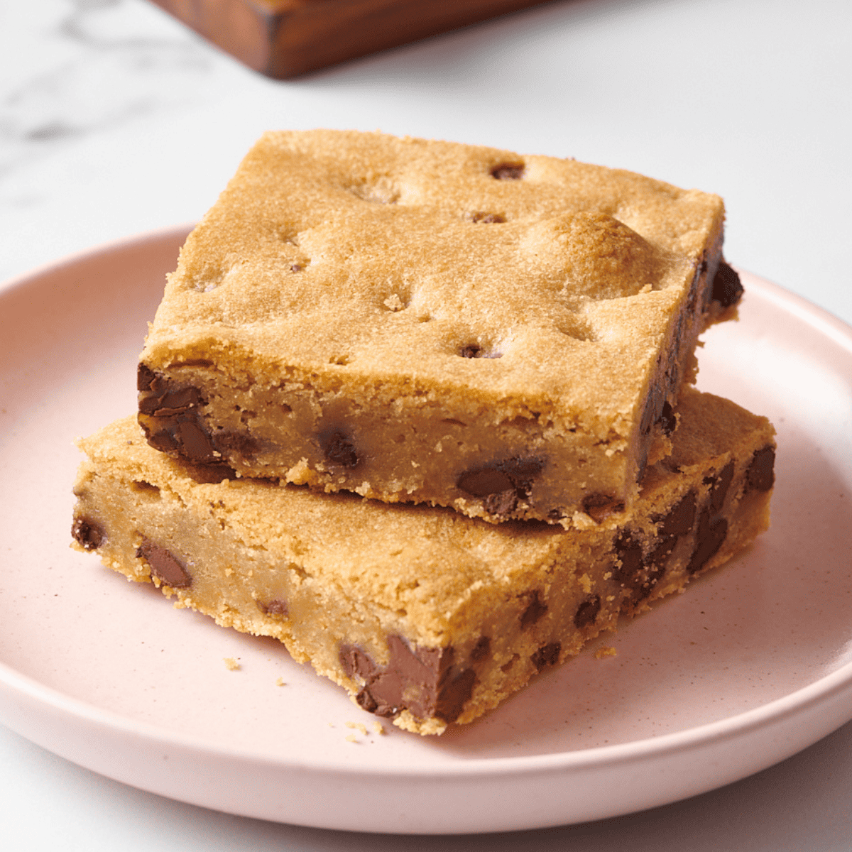Two chocolate chip cookie bars stacked on a pink plate.