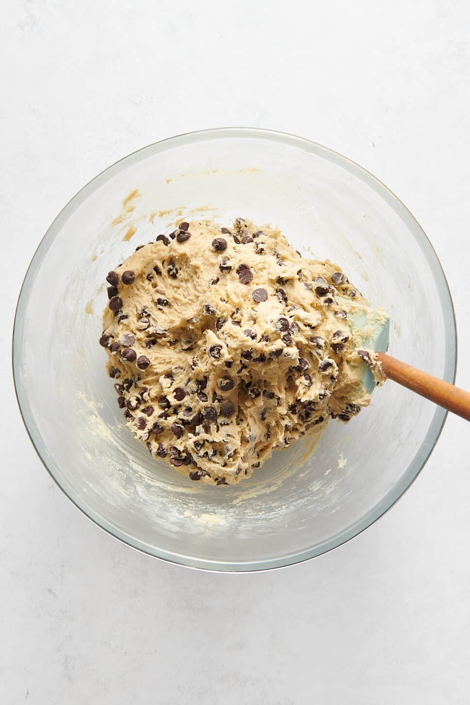 chocolate chip cookie bar dough sitting in a large glass bowl with a rubber spatula