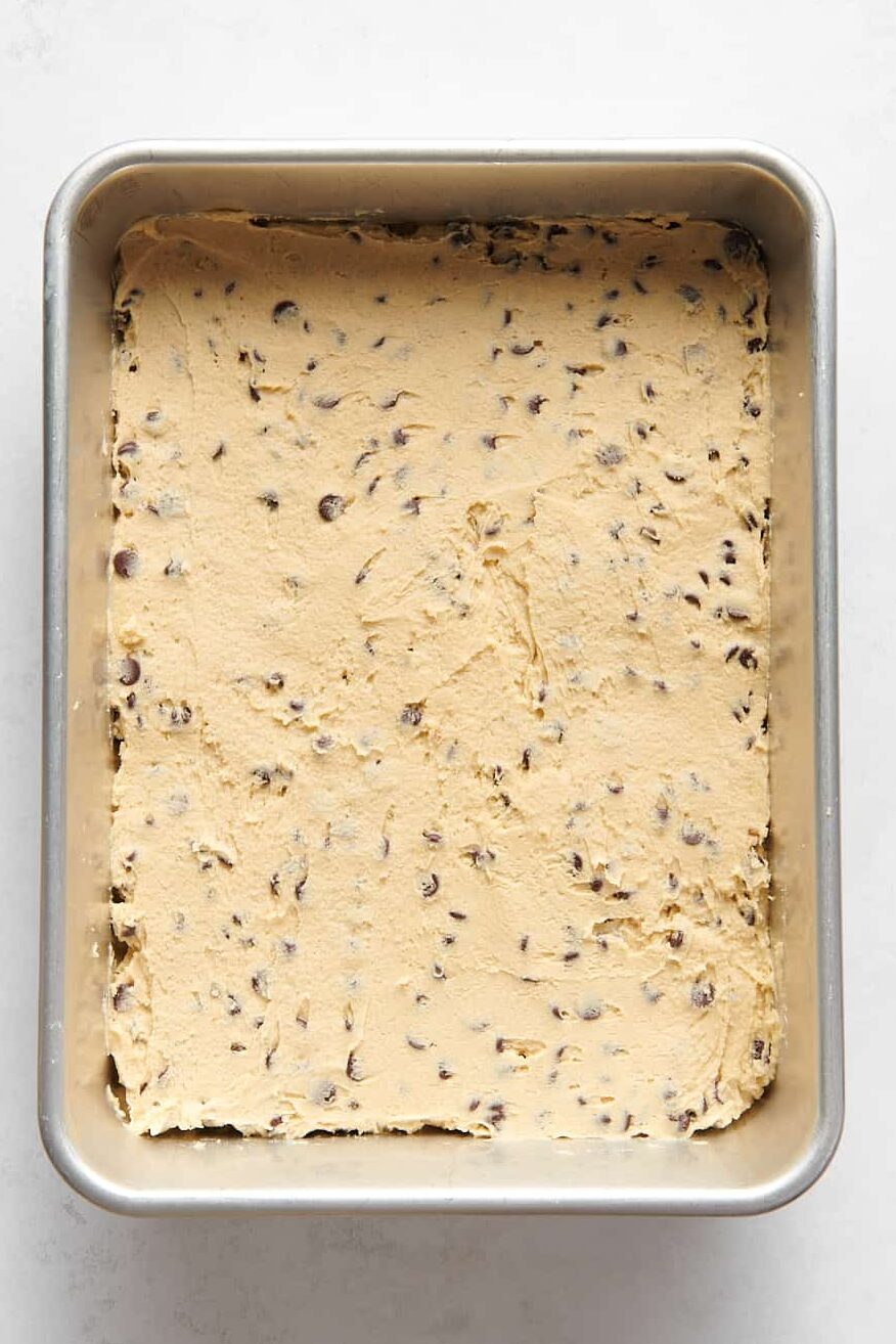 chocolate chip cookie bar dough sitting in a 9x13 baking tray