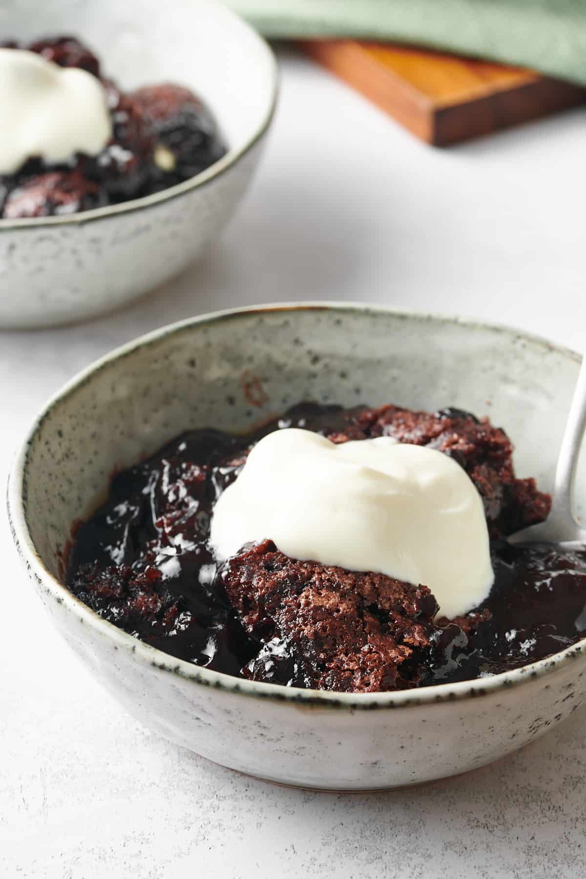 serving of chocolate cobbler served in a speckled ceramic bowl topped with whipped cream