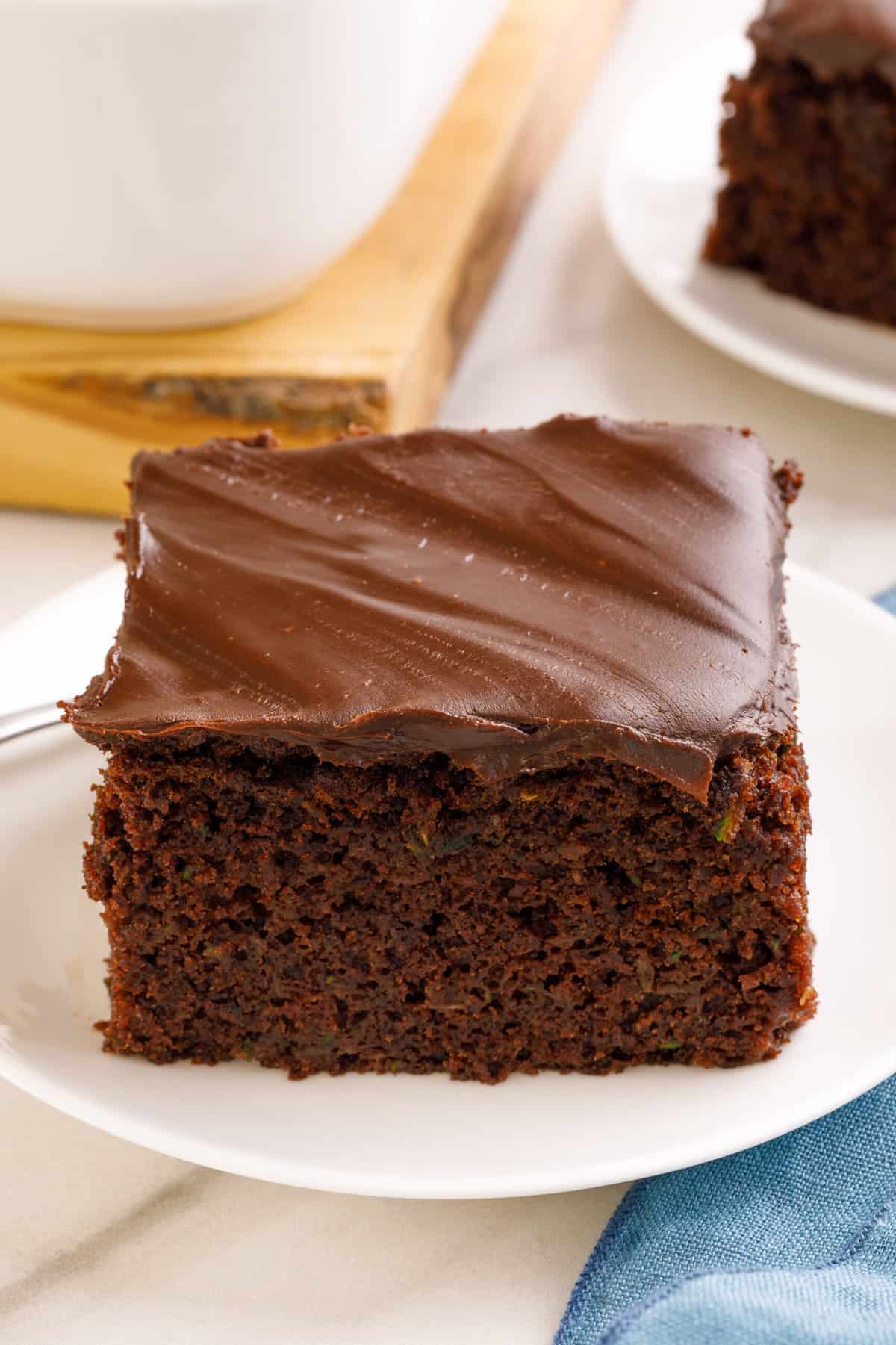 square slice of chocolate zucchini cake sitting on a white round plate