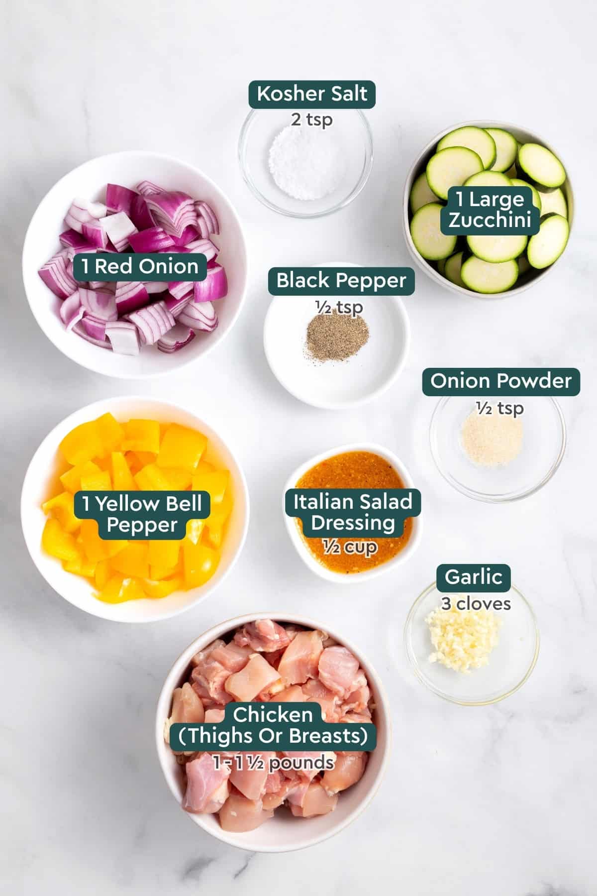 Ingredients for grilled chicken kabobs, including salt, pepper, zucchini, onion, seasonings, Italian dressing, bell pepper, garlic, chicken.