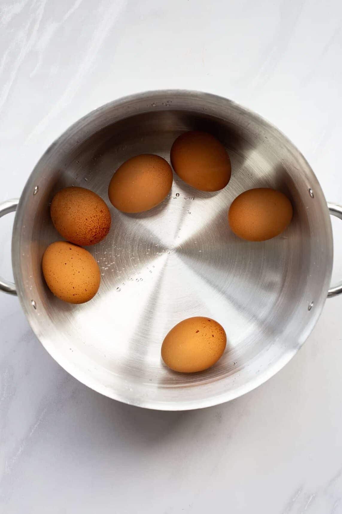stainless steel saucepan with 6 brown hard boiled eggs submerged in water