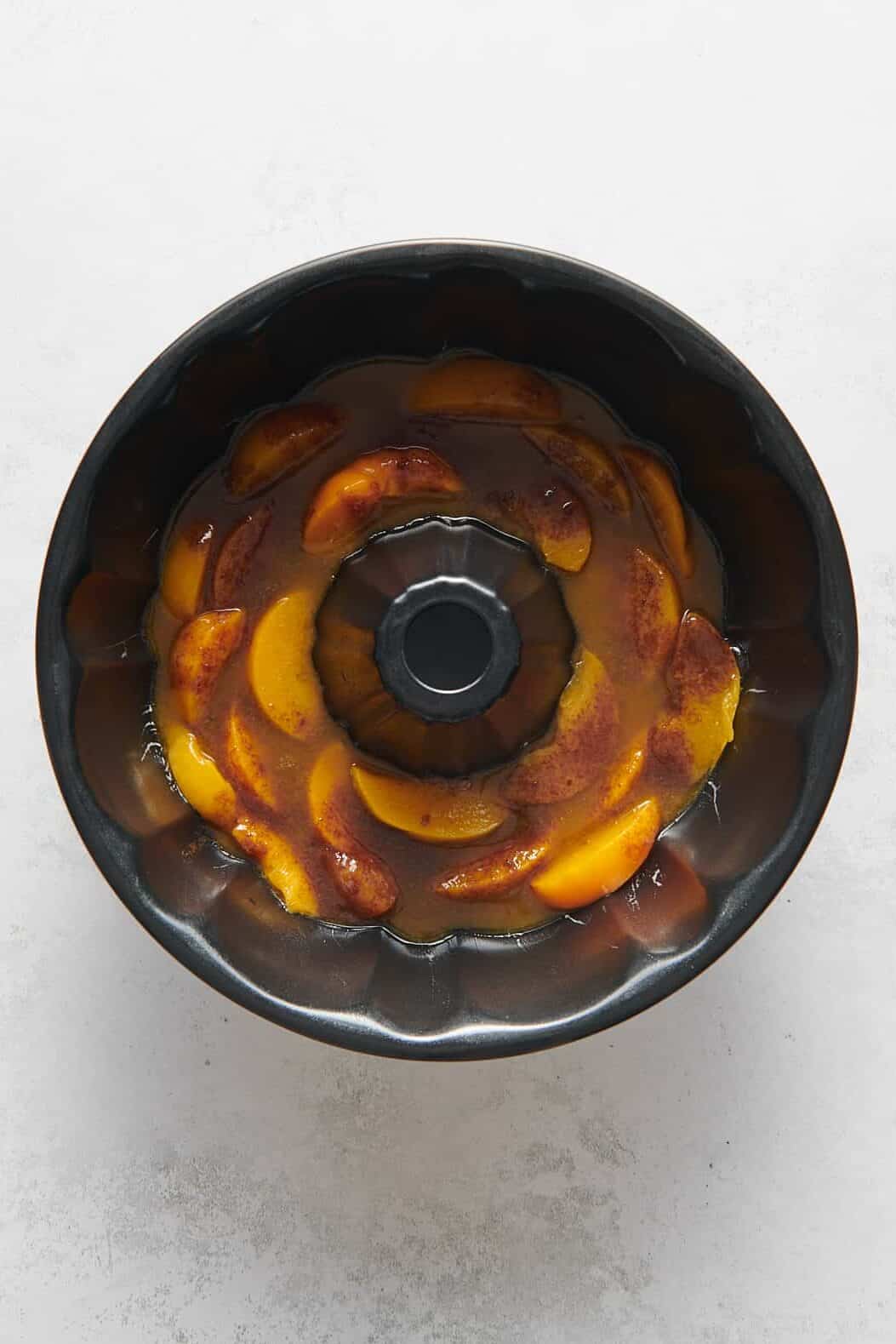 sliced peaches and brown sugar mixture for peach cobbler pound cake prepared at the bottom of a bundt cake pan