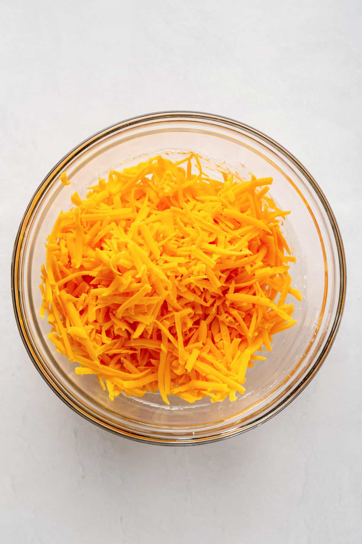 shredded cheddar cheese in a large glass bowl.